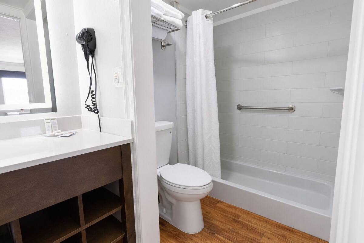 Une salle de bain avec un lavabo blanc, un sèche-cheveux, des toilettes et une douche avec un rideau blanc.