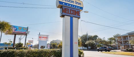 A Destin Inn & Suites sign with a 'WELCOME' message, surrounded by various commercial signs and a clear sky.