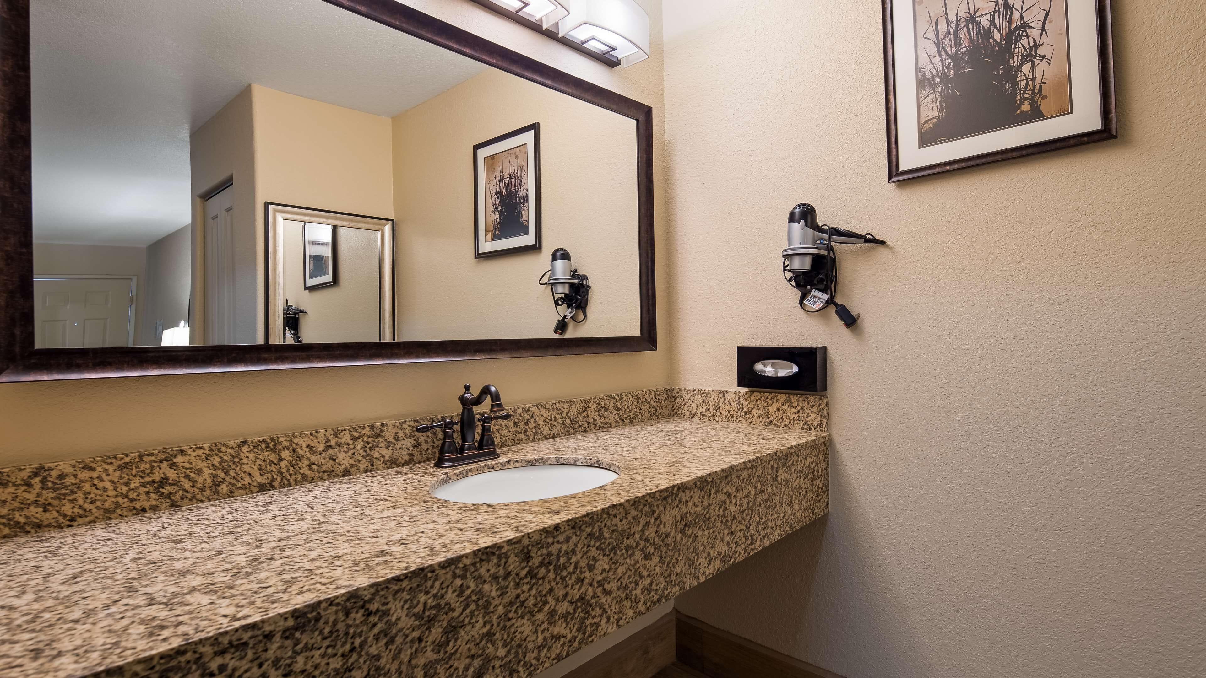 A bathroom with a granite countertop, a sink, a mirror, and a wall-mounted coffee machine.