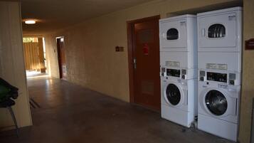 A laundry room with two stacked front-loading washers and dryers, a wooden door, and a hallway leading to another room.