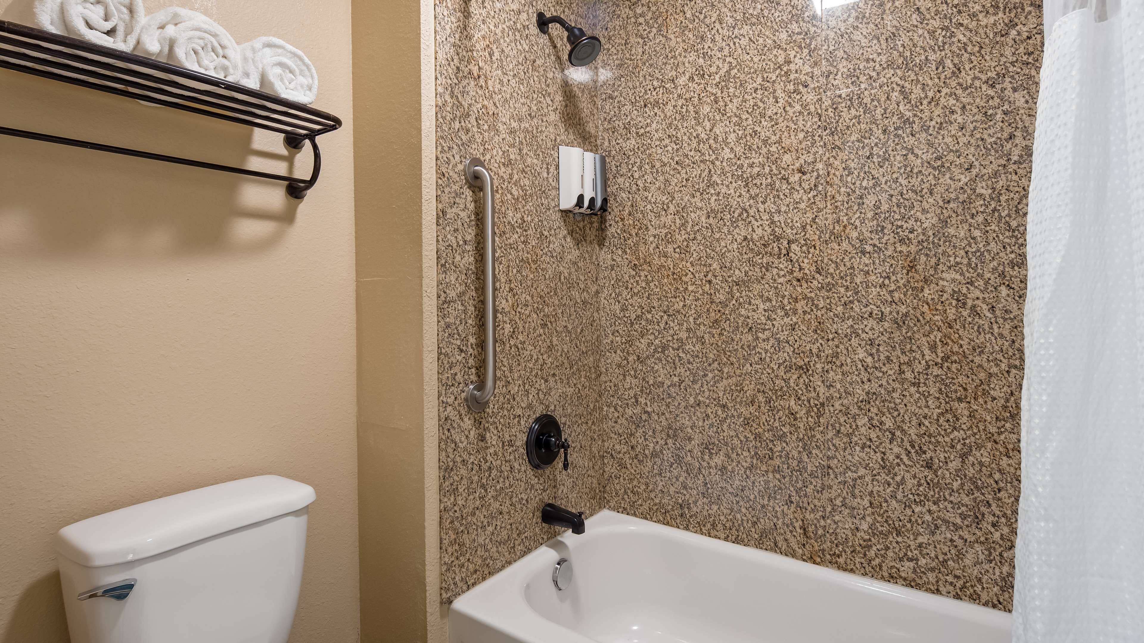 A bathroom with a white bathtub, a shower with a handheld showerhead, a toilet, and a towel rack with towels.