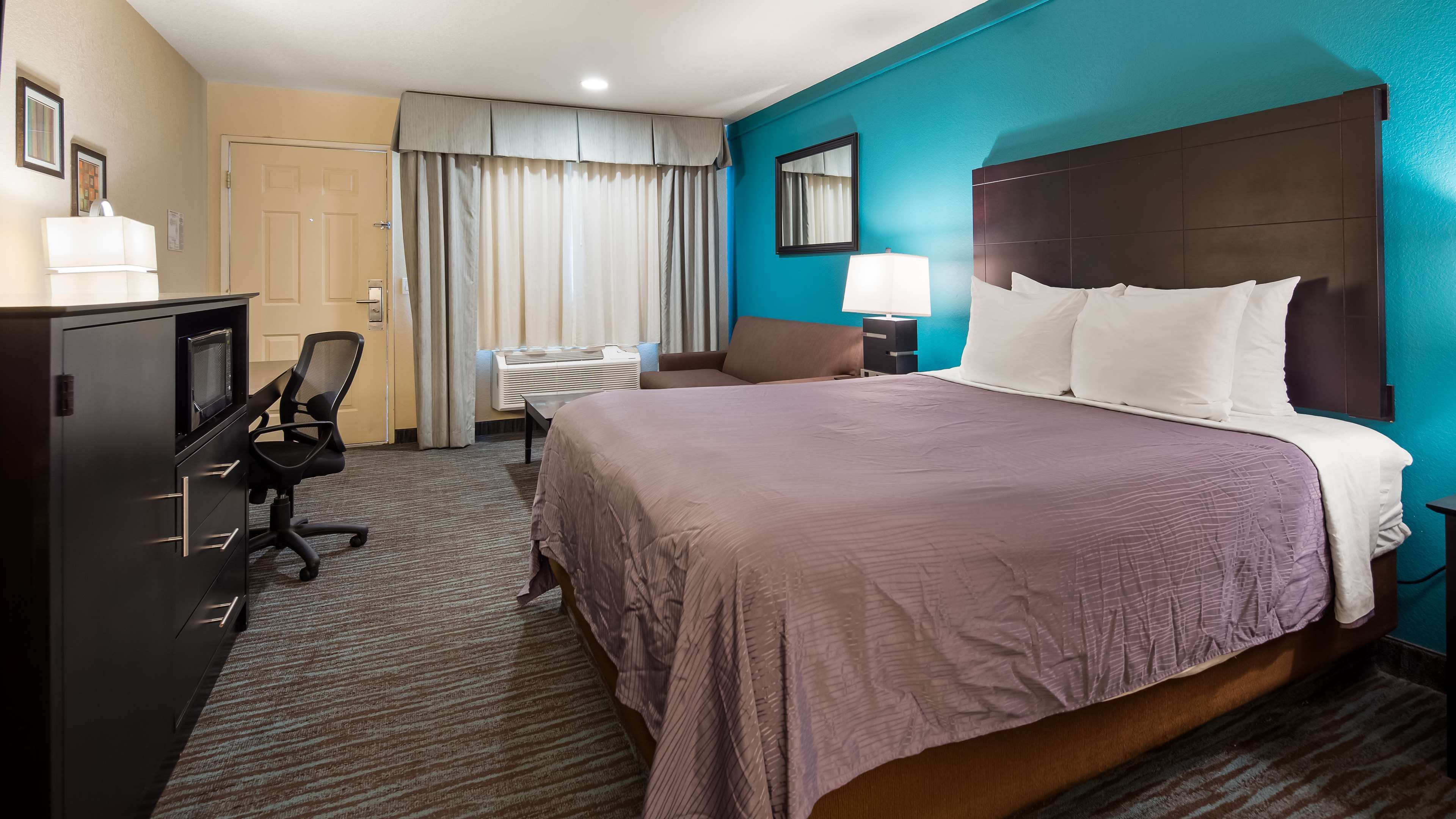 A hotel room with a large bed, a desk with a chair, a TV, and a minibar.