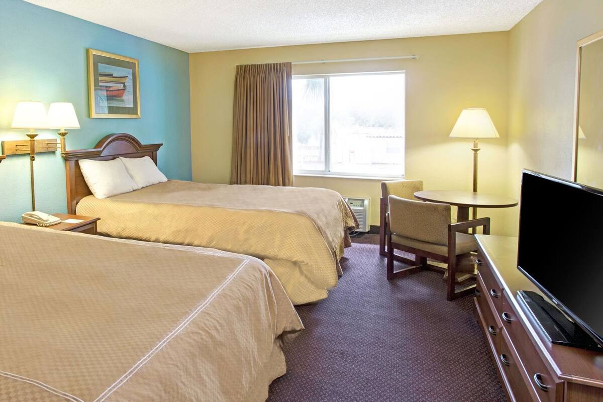 Habitación de hotel con dos camas, un escritorio con silla, televisor y ventana con cortinas.