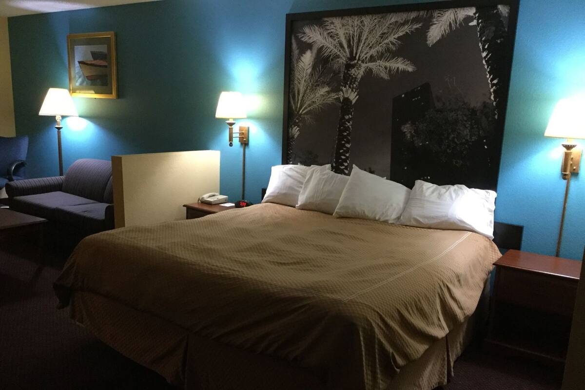 Habitación de hotel con una cama grande, dos mesitas de noche, un sillón y dos lámparas de pared.