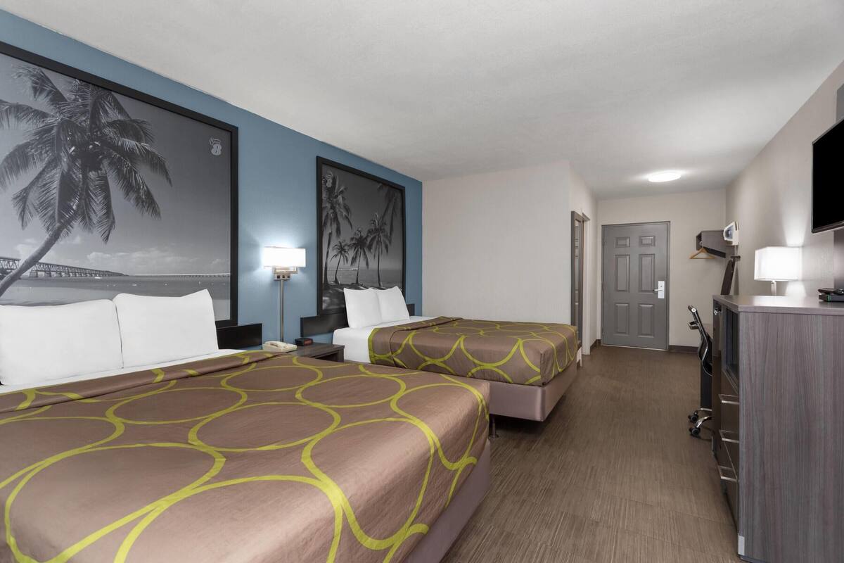 Una habitación de hotel con dos camas, un escritorio, un televisor y una puerta.
