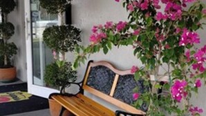 Un banco en un balcón con plantas en macetas y una puerta.