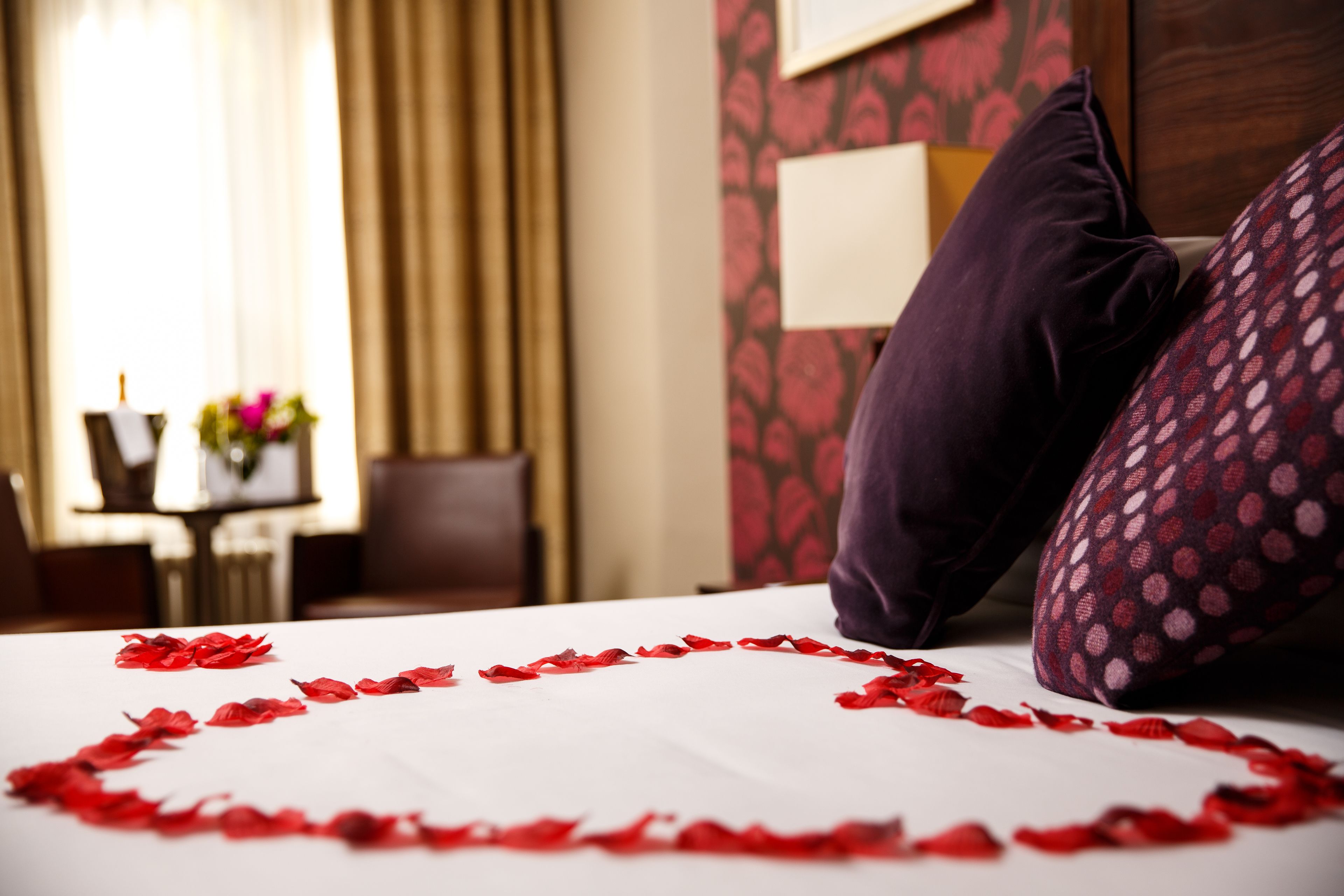 Une chambre d’hôtel avec un lit recouvert de pétales de rose, un oreiller violet et un autre oreiller à motifs.