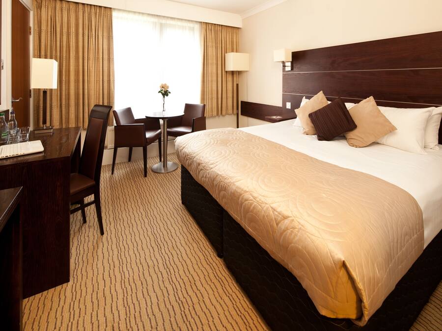 A hotel room with a large bed, a desk with a laptop, a chair, and a television.