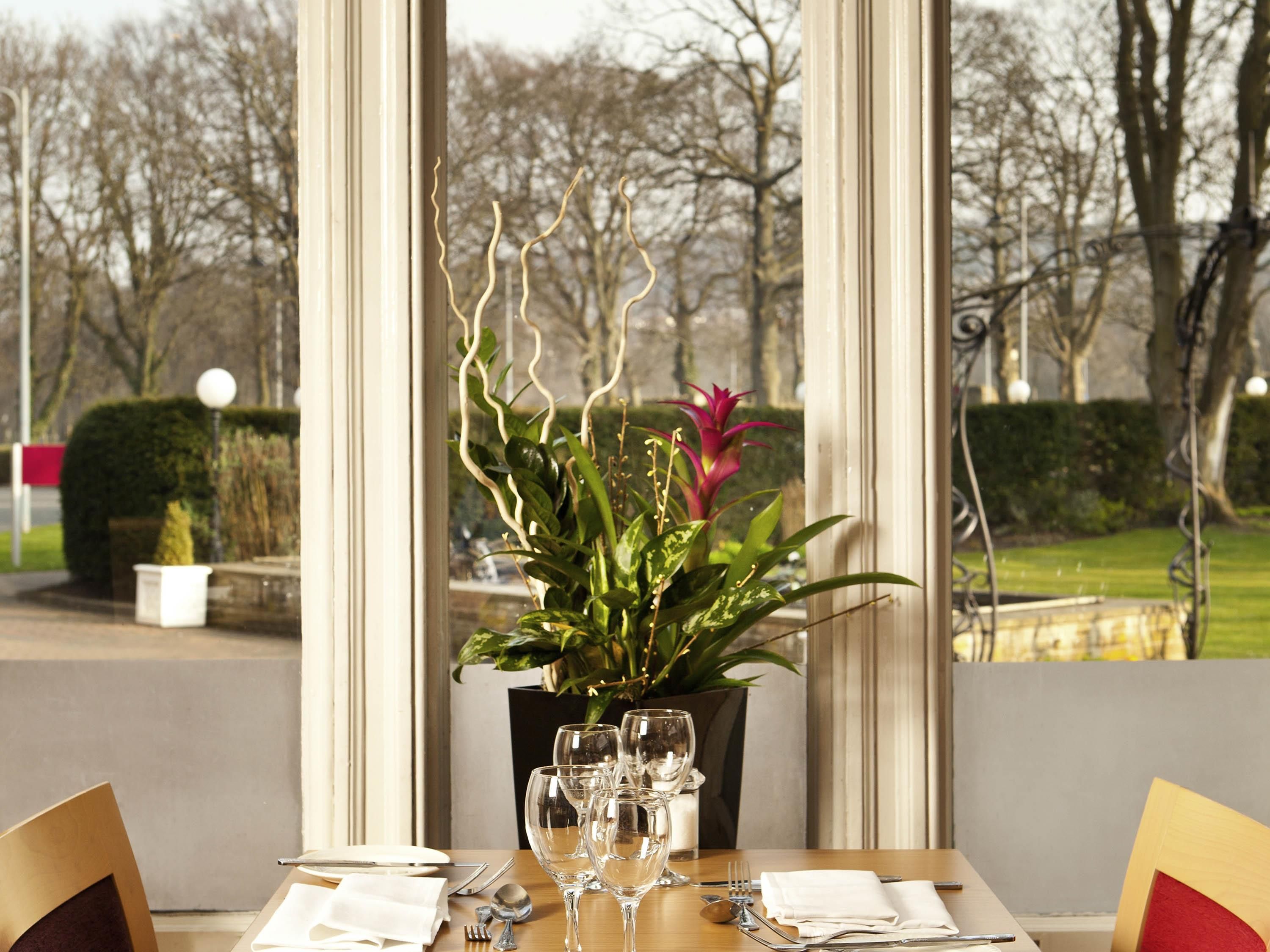 A dining table set with glasses, cutlery, and a potted plant with long, thin leaves.