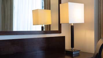 A hotel room with a wooden headboard, a bedside table, a lamp, and a mirror reflecting the room.