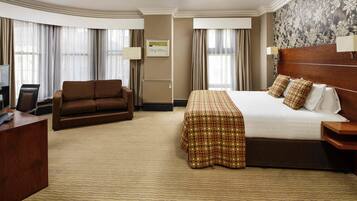 A hotel room with a bed, a sofa, a desk, and a television.