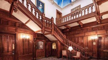 A grand staircase with intricate woodwork, a chandelier, and a patterned carpet.