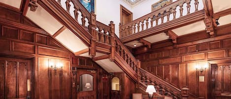 Una gran escalera con detalles tallados, un candelabro y una alfombra estampada.