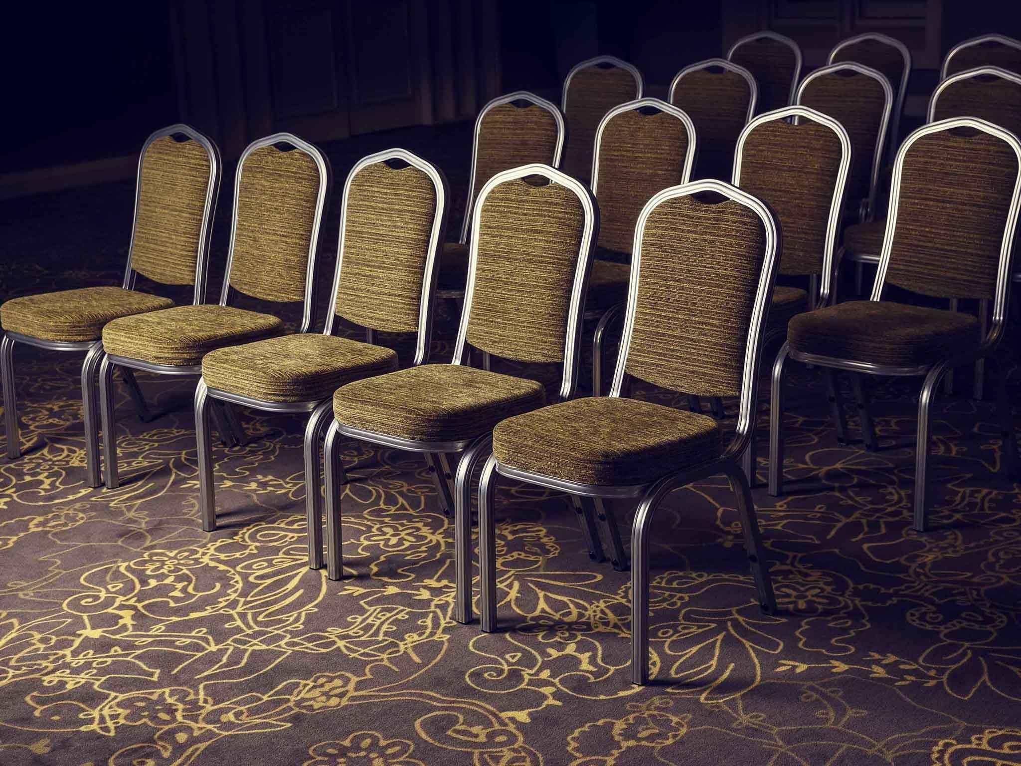 Des rangées de chaises aux assises en osier et aux structures métalliques, disposées sur un tapis à motifs floraux.