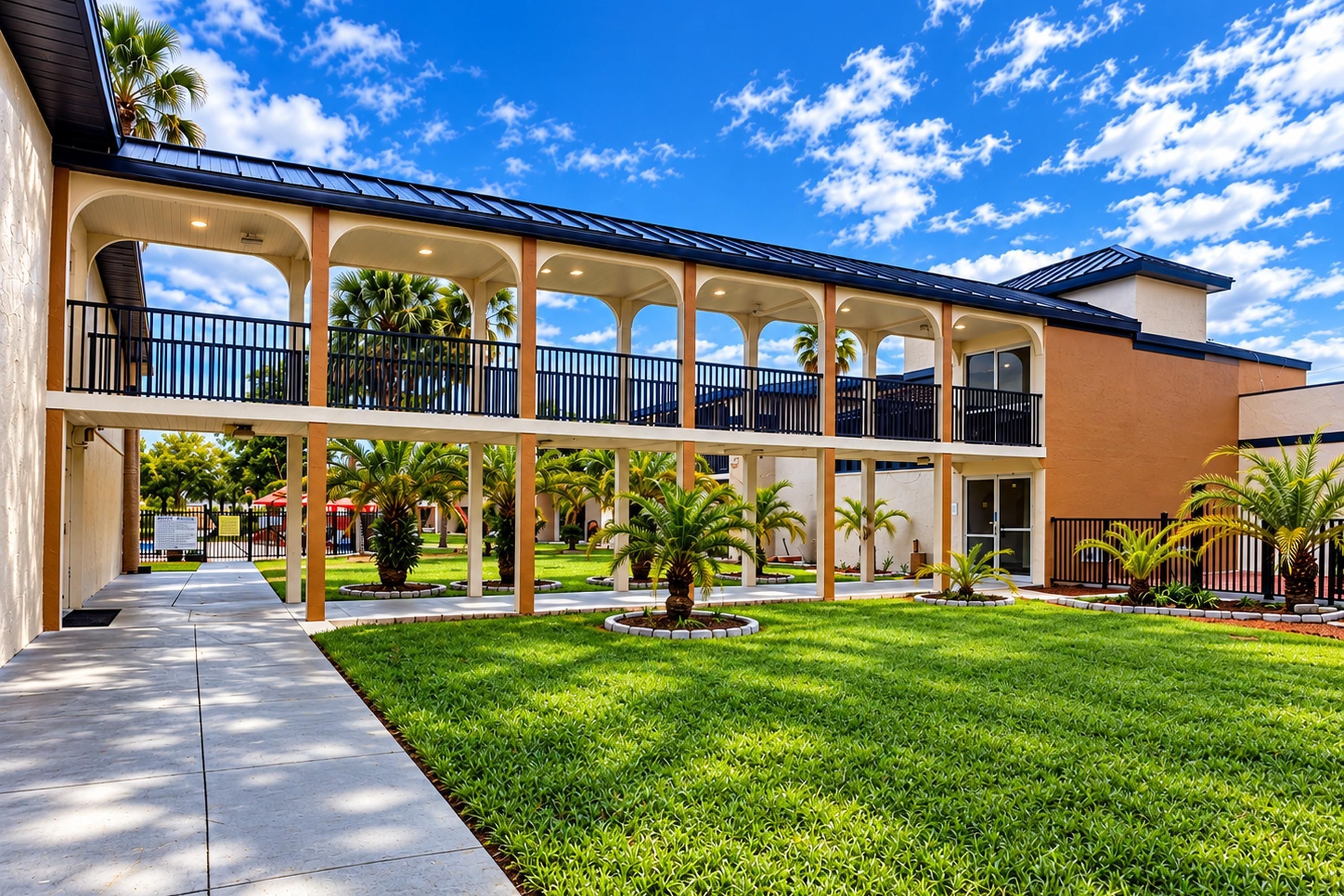 A multi-story building with a covered courtyard, palm trees, and a clear blue sky.