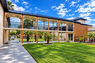 Un edificio a più piani con un cortile coperto, palme e un cielo azzurro intenso.