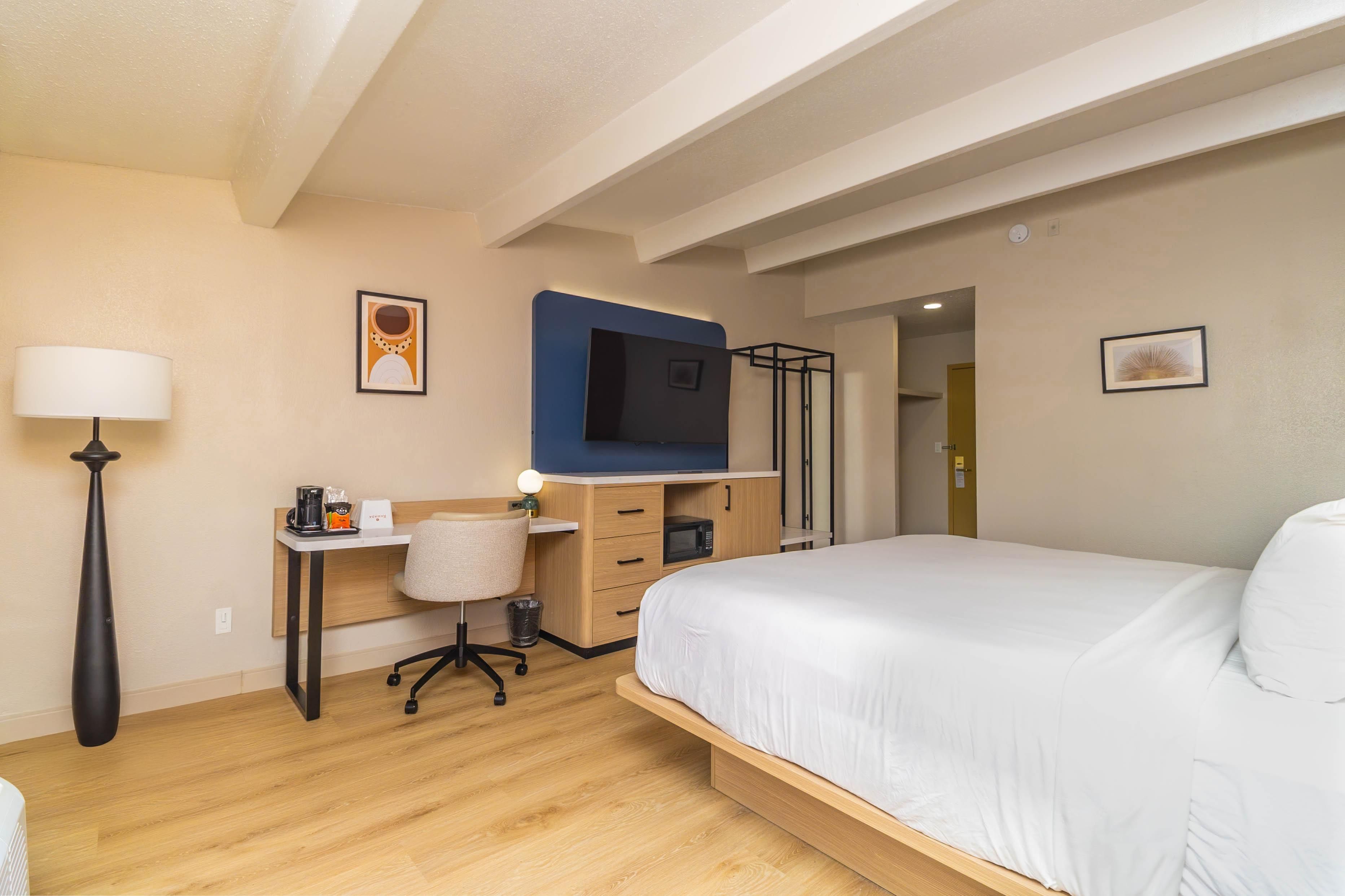 A hotel room with a bed, desk, chair, lamp, and a television.