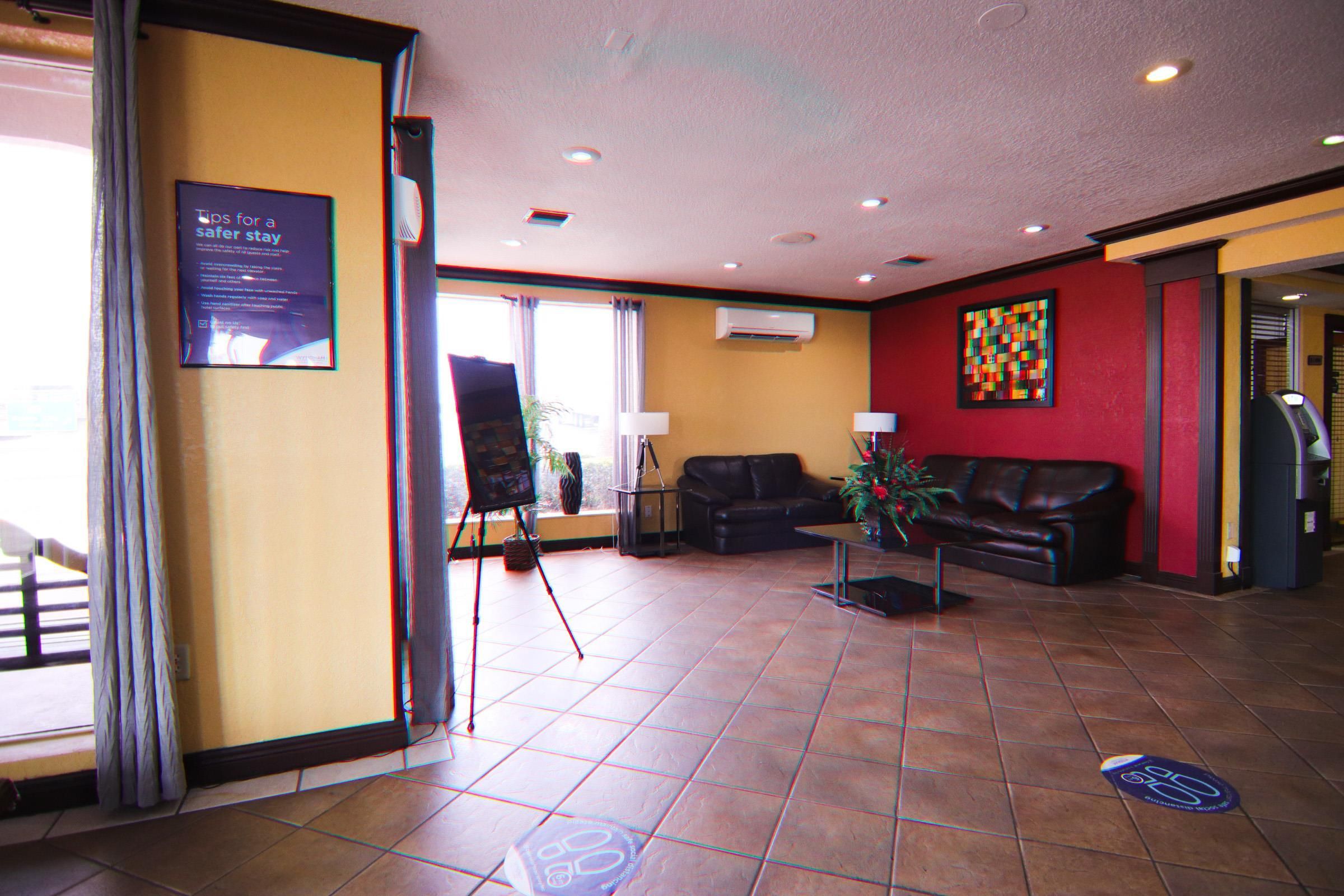 A hotel lobby with a black leather sofa, a standing easel, and a colorful abstract painting on the wall.