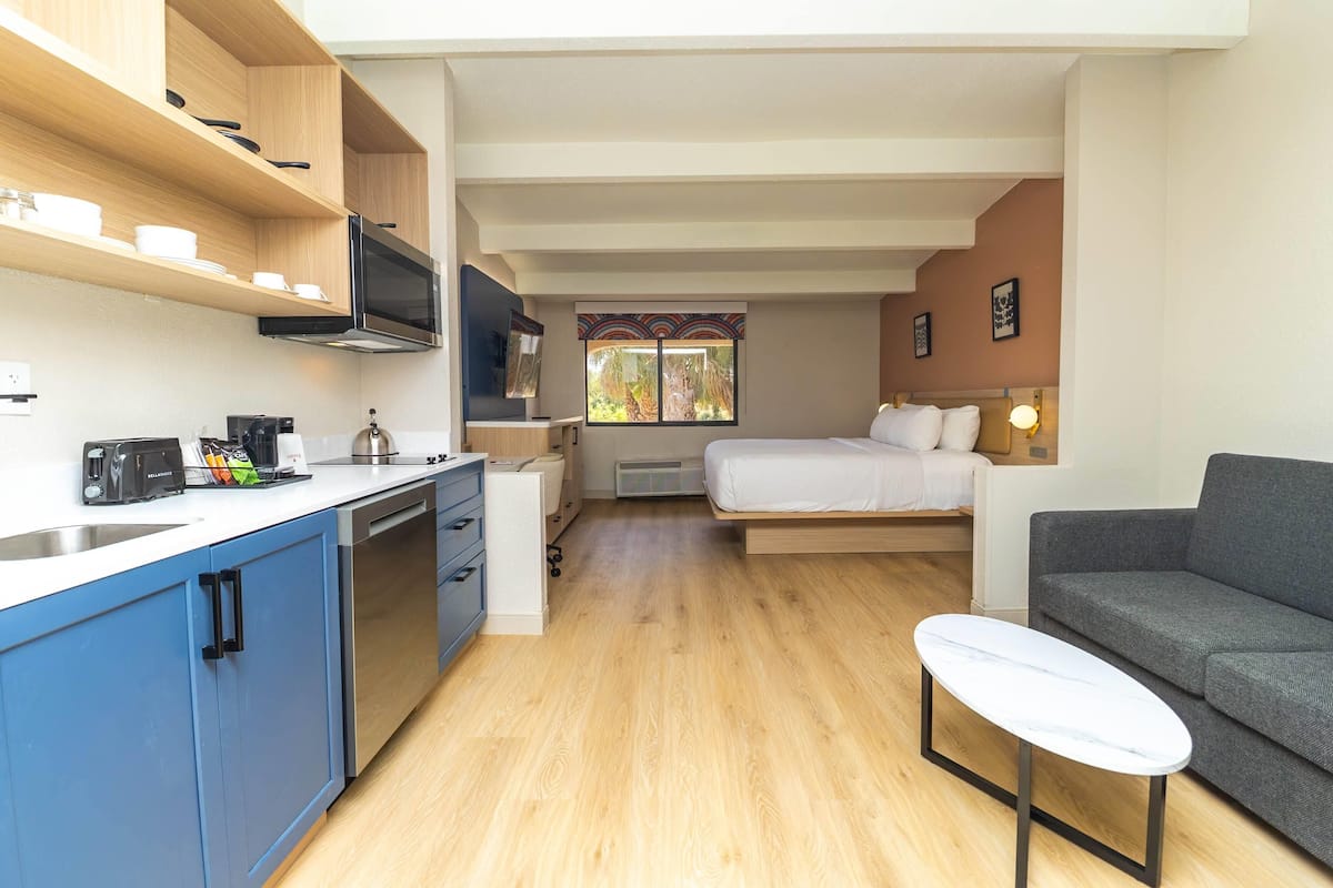 A compact room with a kitchenette, a bed, a sofa, and a small table.