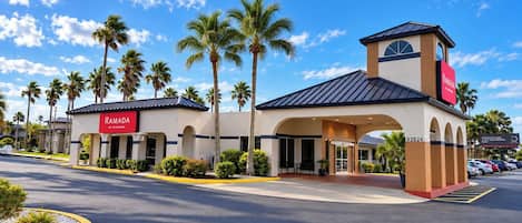 A hotel with a prominent entrance, palm trees, and a clear blue sky.