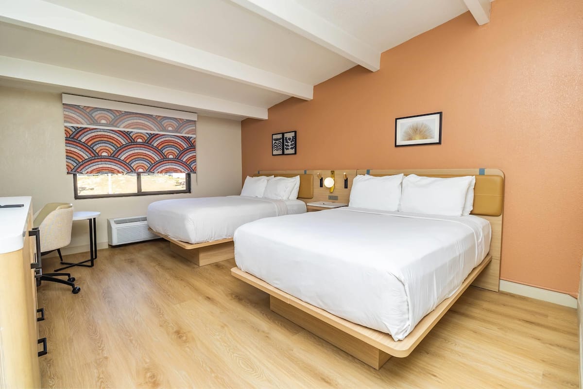 A hotel room with two beds, a desk, and a large window with a colorful view.