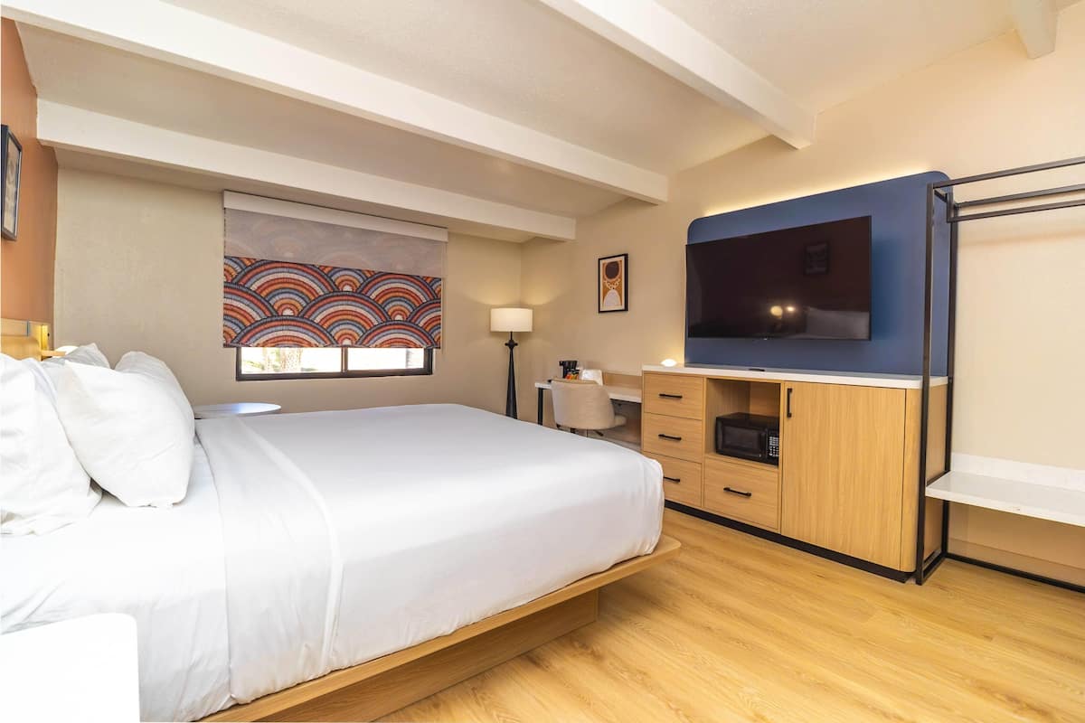 A bedroom with a bed, a desk, a TV, and a window with a colorful view.