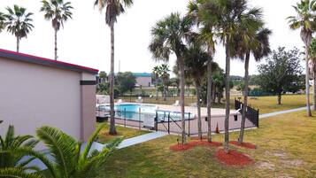 A pool area with a fenced pool, palm trees, and a building with a red roof.