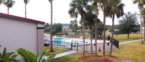 A pool area with a fenced pool, palm trees, and a building with a red roof.