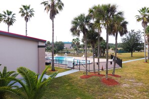 A pool area with a fenced pool, palm trees, and a building with a red roof. - Ramada by Wyndham Davenport Orlando South (Davenport)