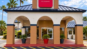 A Ramada hotel with a red sign, a covered entrance, and palm trees in the background.