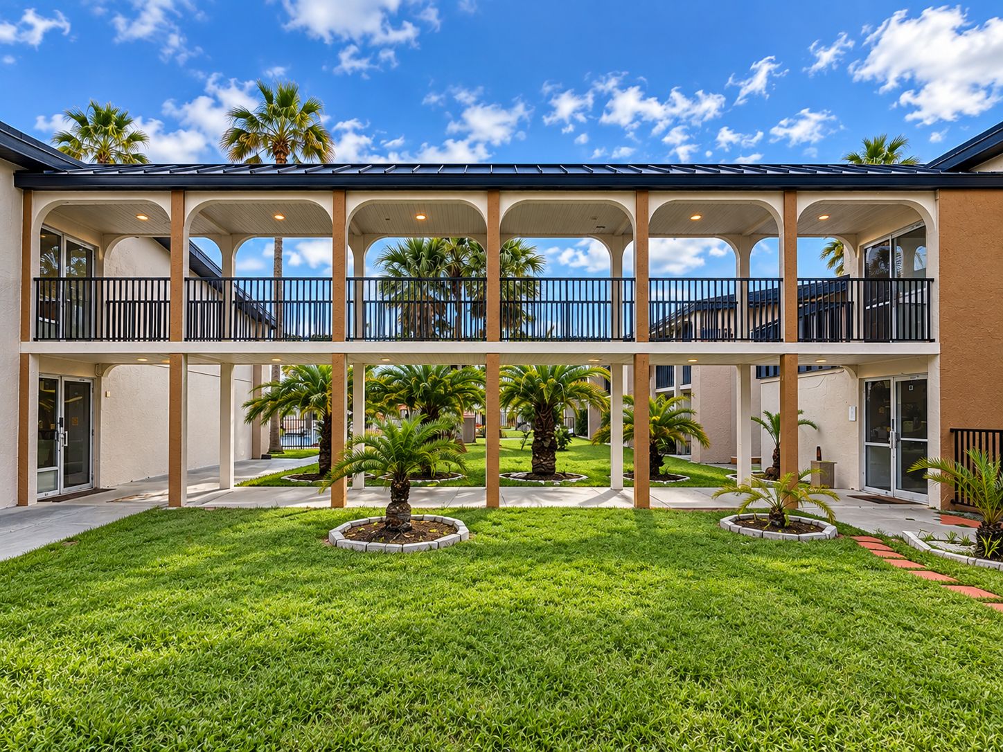 A two-story building with a covered courtyard, palm trees, and a clear sky.