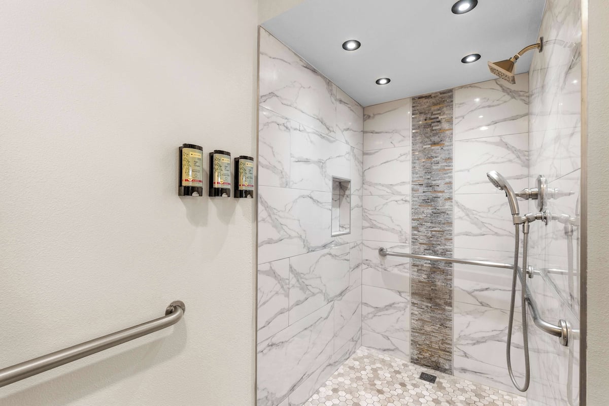 A modern shower with a glass door, a handrail, and a tiled floor.