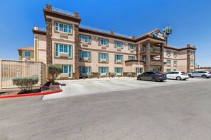 Un hotel de varios pisos con fachada color beige, múltiples balcones y un estacionamiento con varios automóviles.