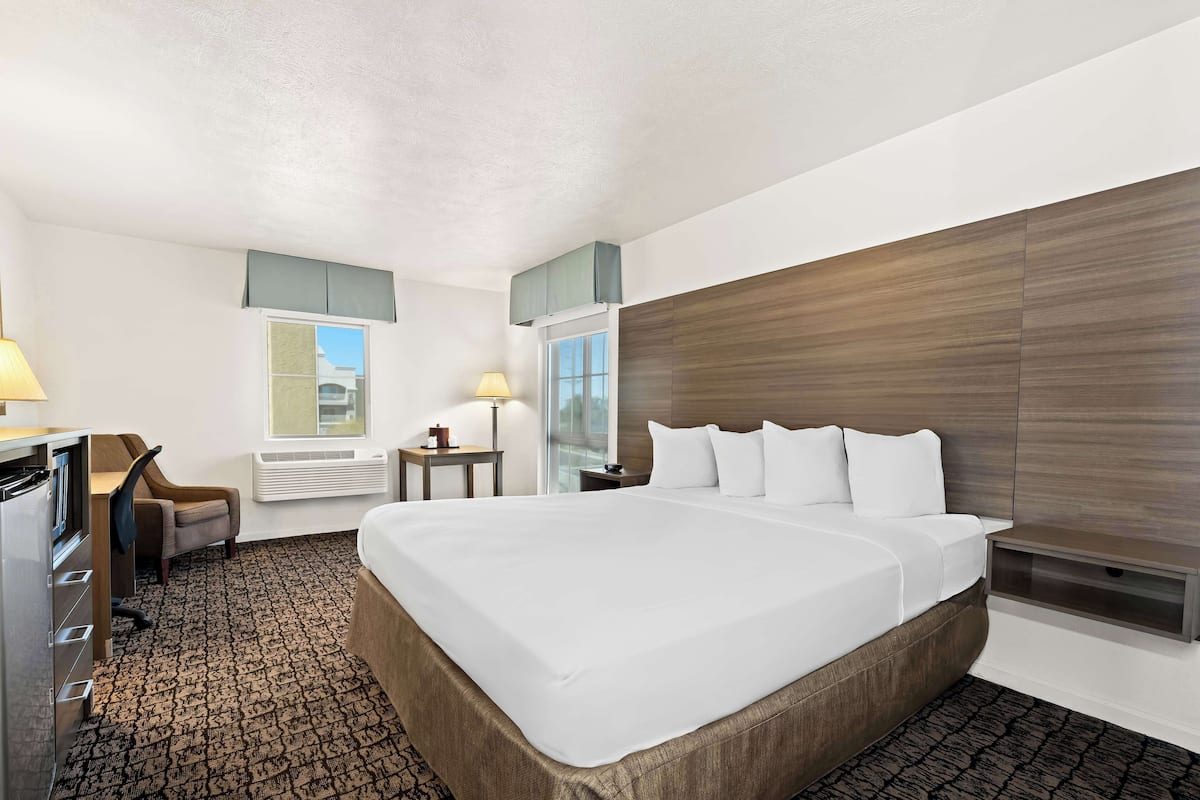 A hotel room with a large bed, a desk, a chair, a lamp, and a window.