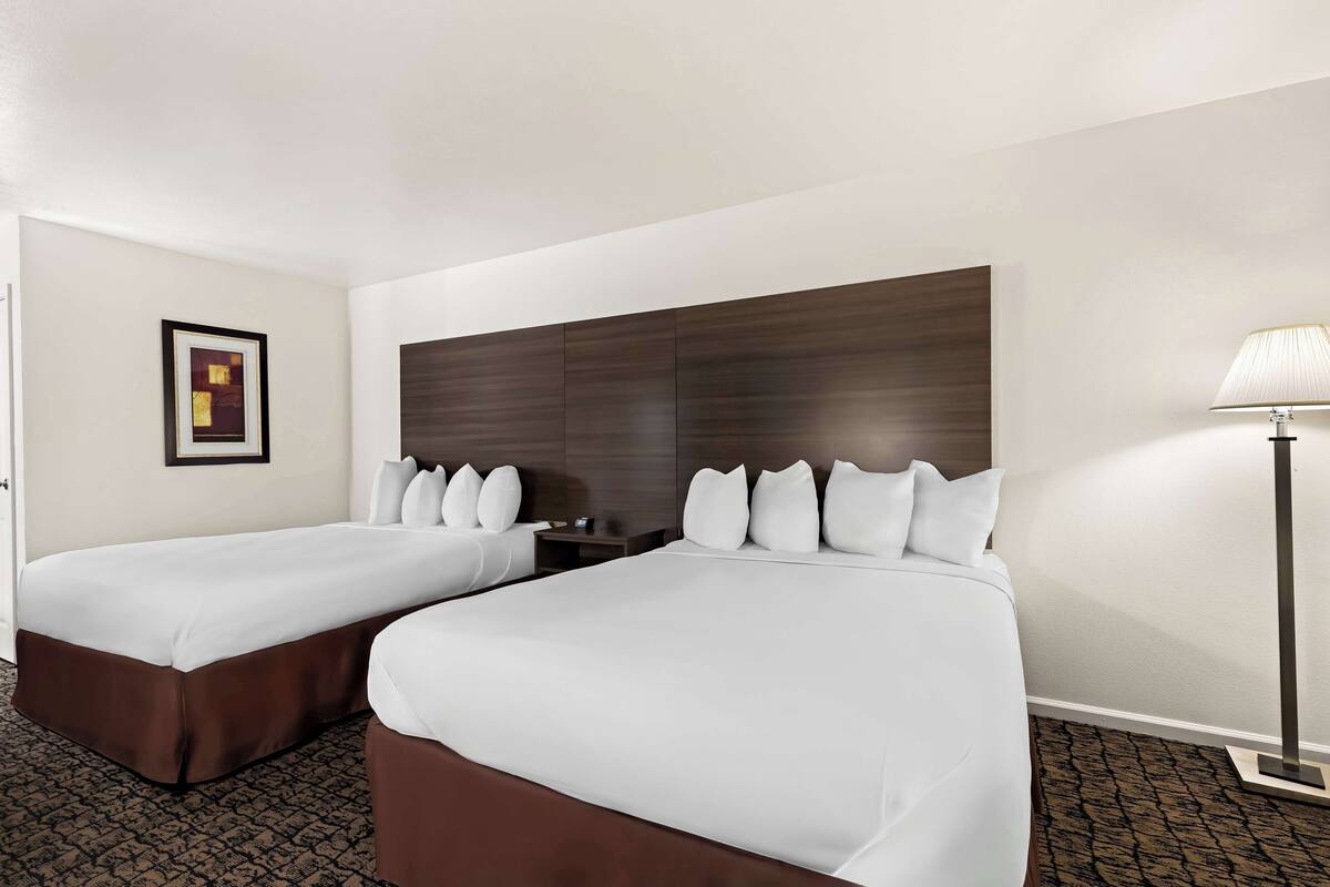 A hotel room with two beds, a dark headboard, a framed picture on the wall, and a floor lamp.