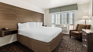 Ein Hotelzimmer mit einem großen Bett, einem Schreibtisch, einem Stuhl, einer Lampe und einem Fenster mit Jalousien.