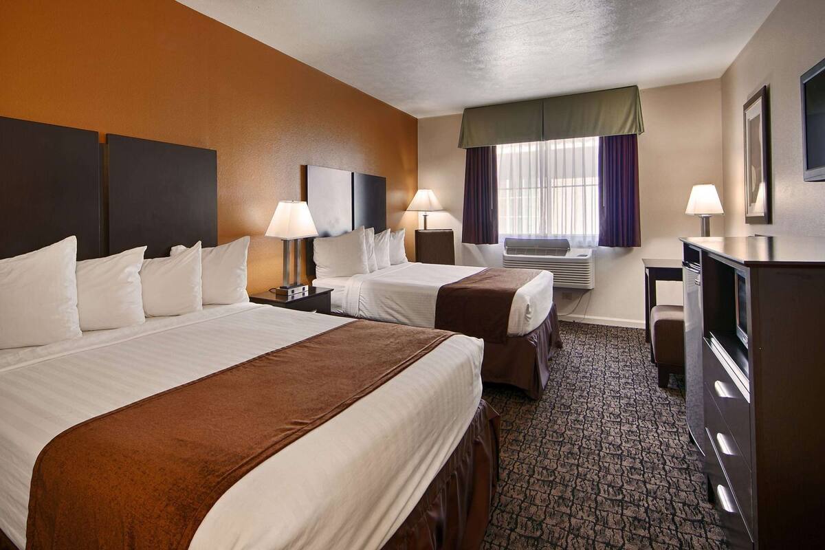 A hotel room with two beds, a desk, a TV, and an air conditioning unit.