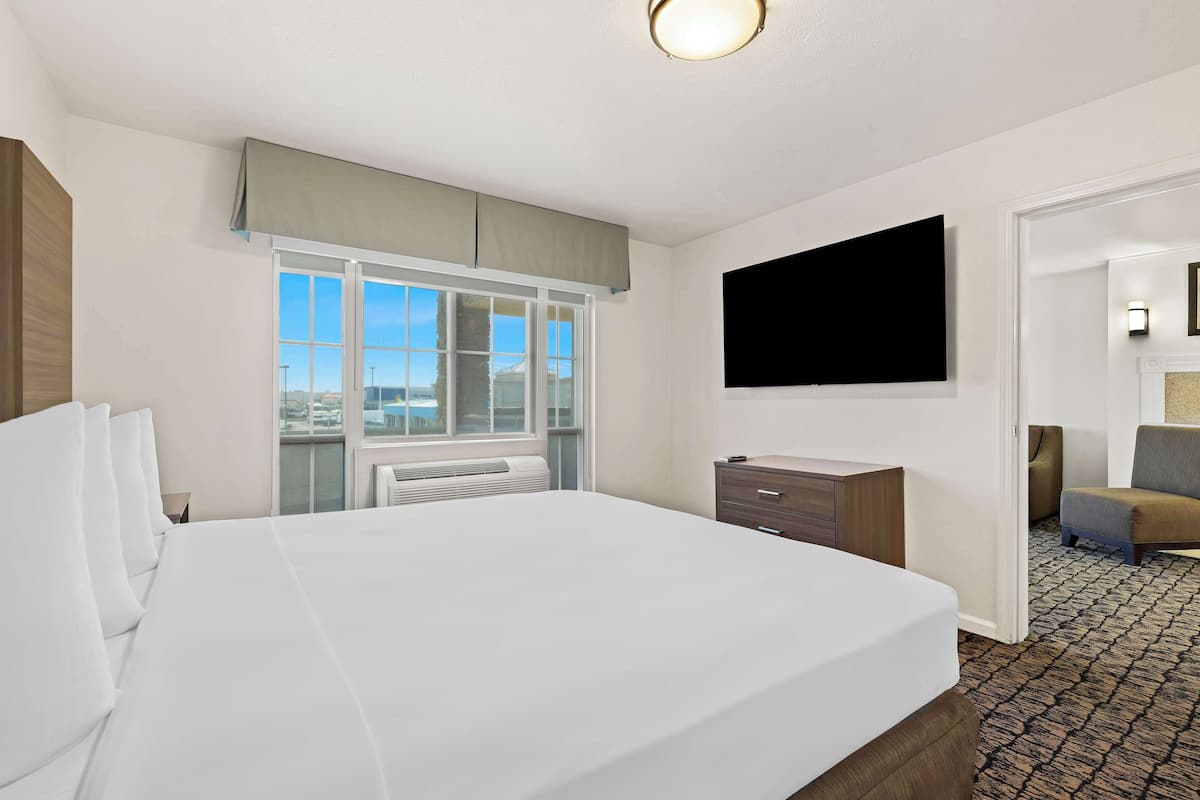 A hotel room with a large bed, a flat-screen TV mounted on the wall, a window with a view, and a small desk with drawers.