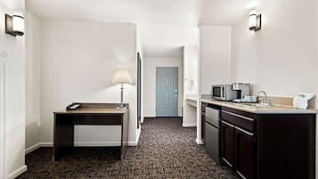 Habitación de hotel con escritorio, lámpara, microondas, lavamanos y puerta que da a otra habitación.