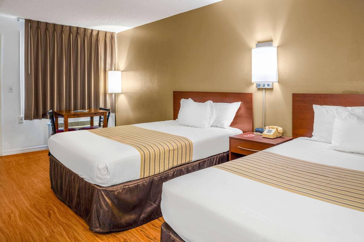 A hotel room with two beds, a wooden table, a lamp, and a telephone on the nightstand.