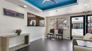A hotel lobby with a dark wood floor, a reception desk, a seating area with two chairs, a large mirror, and a ceiling fan. - Days Inn by Wyndham Downey (Downey)