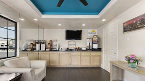A modern kitchen with a flat-screen TV, a Daybreak coffee station, and a beige sofa. - Days Inn by Wyndham Downey (Downey)