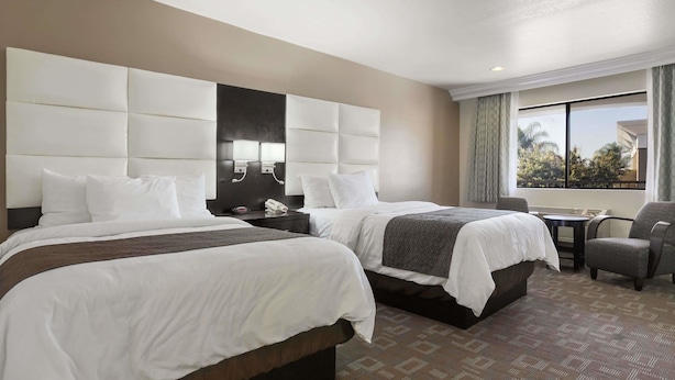 A hotel room with two beds, a large padded headboard, a small table, and a chair. - Days Inn by Wyndham Downey (Downey)