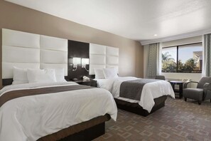 Habitació d'hotel amb dos llits, un capçal gros i amb abundant farciment, una taula petita i una cadira.