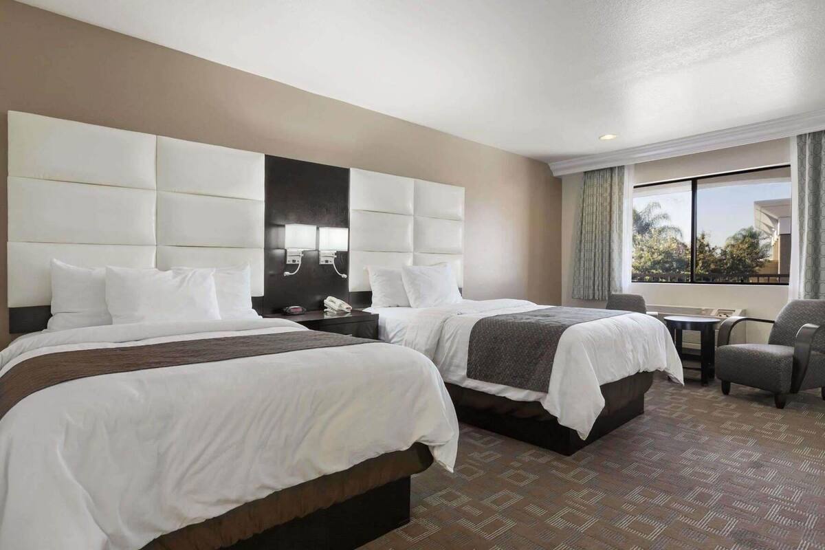 A hotel room with two beds, a desk, a chair, a large mirror, and a window with a view.