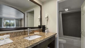 A bathroom with a granite countertop, a sink, a mirror, a hairdryer, a toilet, and a shower. - Days Inn by Wyndham Downey (Downey)