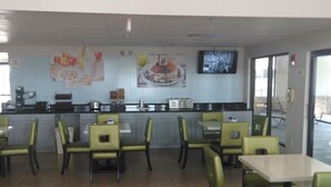 A restaurant with a counter, chairs, and tables. There are paintings on the wall and a television screen.