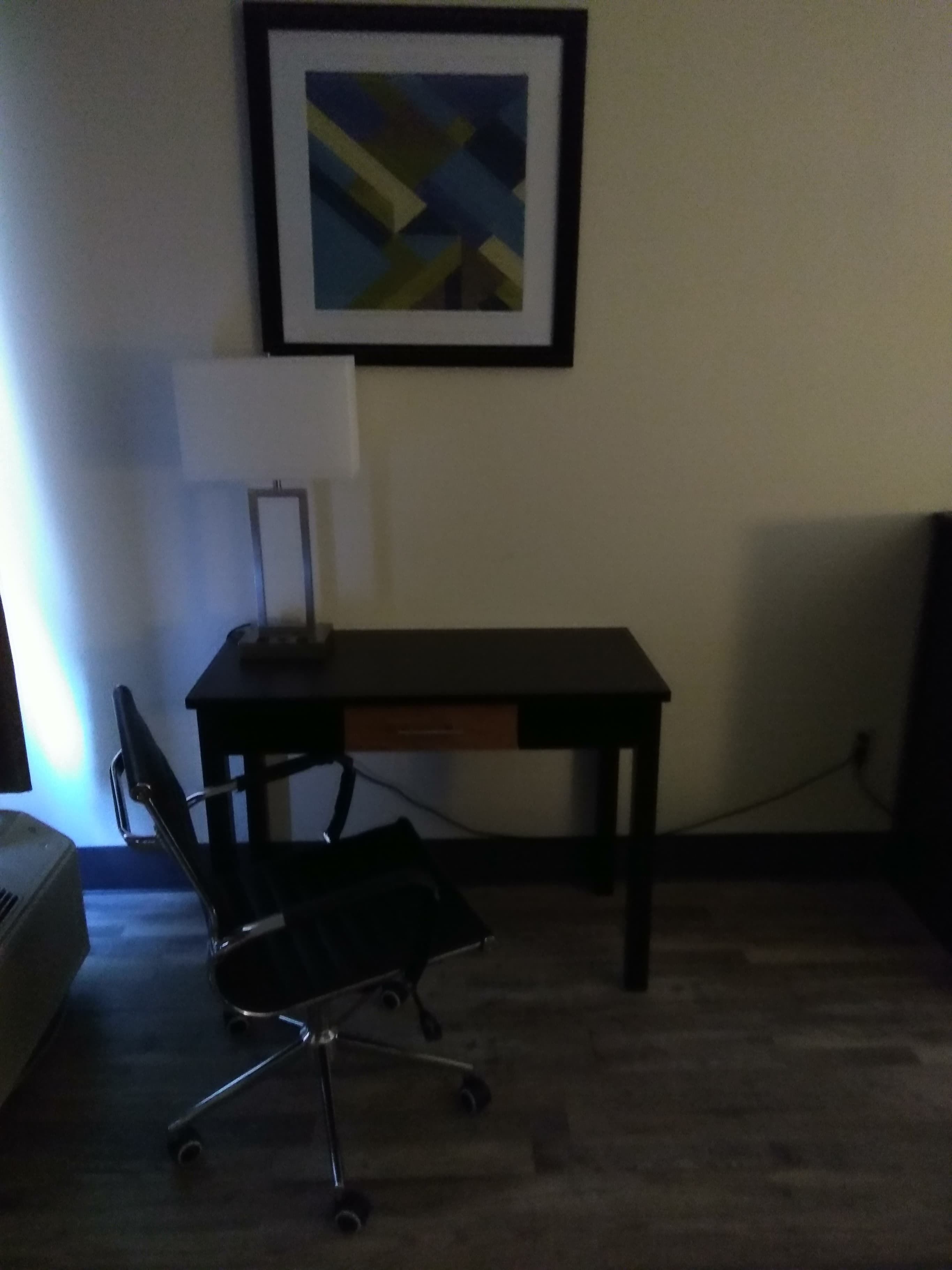 Un petit bureau comprenant un bureau, une chaise et une œuvre d’art encadrée accrochée au mur.