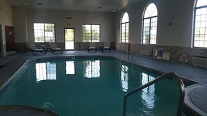 An indoor swimming pool with clear glass walls, a pool ladder, and lounge chairs.