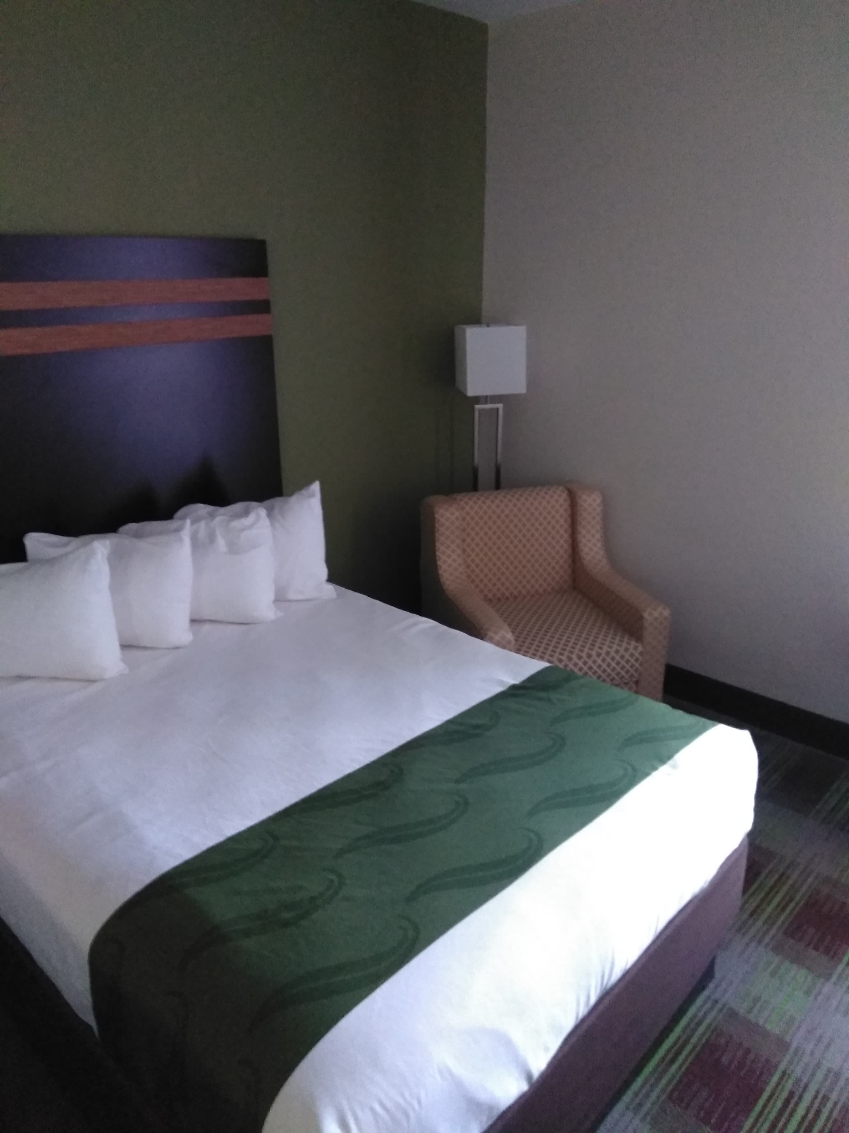 A hotel room with a large bed, a chair, and a lamp.